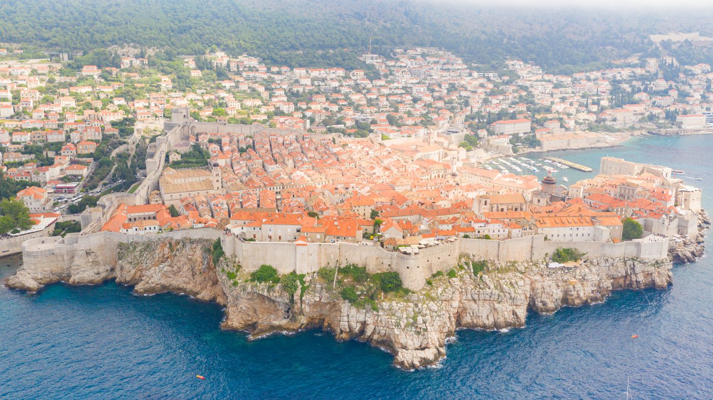 Den gamle bys mur i Dubrovnik set fra havsiden — stejl kyst og terrakotta-tage