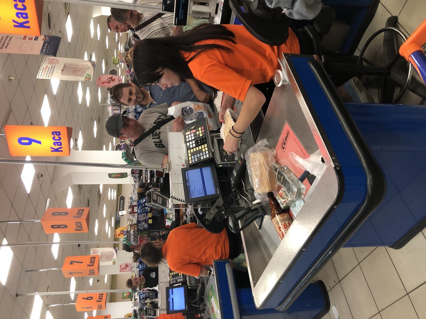 A supermarket checkout area with shoppers waiting in line, baskets on the conveyor belt